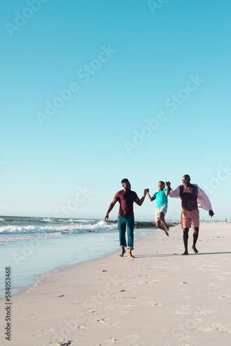 Cheerful african american father and grandfather holding boy's hands and picking him up at beach