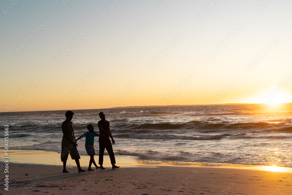 Silhouette african american boy with mother and father walking on beach against sky at sunset