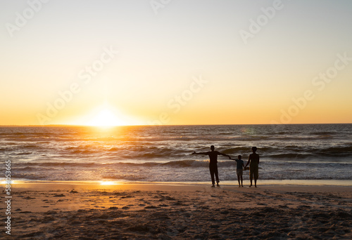 Silhouette african american son holding mother and father's hands and standing on beach at sunset