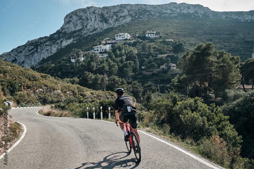 A professional cyclist's epic mountain ride.Male cyclist riding in the mountains.Man cyclist wearing cycling kit and helmet.Beautiful motivation image of an athlete.Descending the mountain.Xàbia,Spain