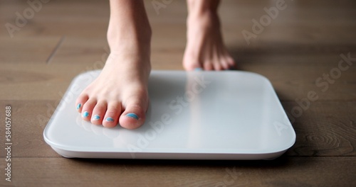 Young girl teenager steps on white scales to measure control weight. Teen checks body mass and fat, healthy dieting and fitness concept. photo