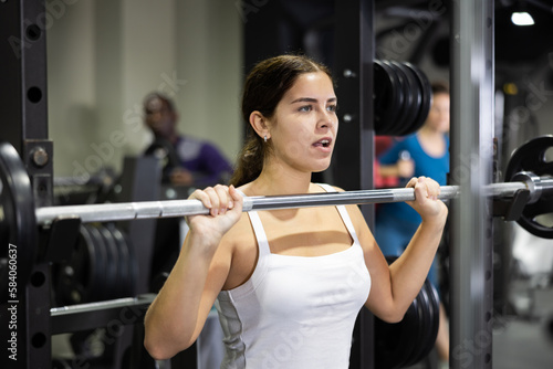 Caucasian woman doing exercises usining barbell and half rack in gym