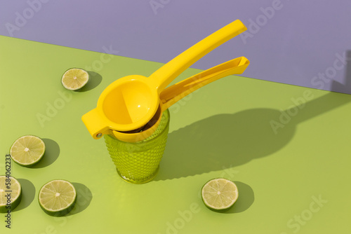 lemon squeezer with fresh limes on green and lavender background, visible shadows, space for text