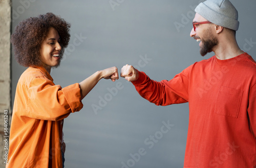 Multiracial couple, team, colleagues sharing a fist bump, smiling standing over gray wall backdrop