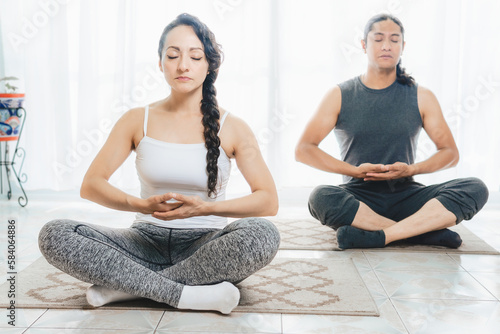 Two people do Yoga indoors, there is plenty of light.