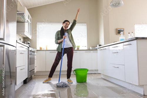 Cheerful caucasian young woman with hand raised dancing, singing and cleaning floor with wet mop photo