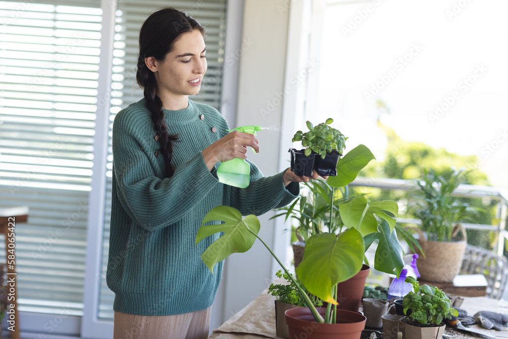 Caucasian beautiful young woman spraying water on potted plants while standing at home, copy space Caucasian beautiful young woman spraying water on potted plants while standing at home, copy space