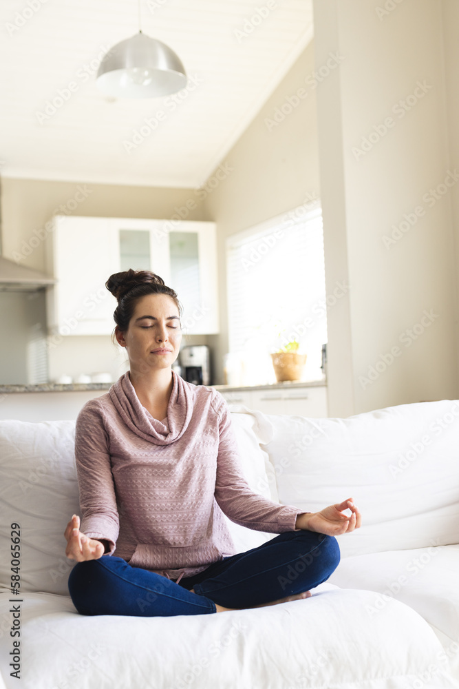 Caucasian young woman meditating while sitting on sofa in living room, copy space Caucasian young woman meditating while sitting on sofa in living room, copy space