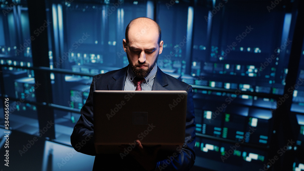 System engineer running hosting server diagnostics with laptop, standing in modern big data center space. IT technician working on professional mainframe hardware. Tripod shot. System engineer running hosting server diagnostics with laptop, standing in modern big data center space. IT technician working on professional mainframe hardware. Tripod shot.