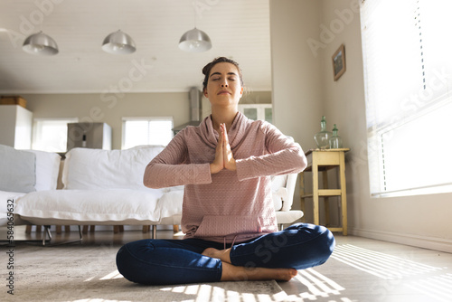 Caucasian young woman meditating in prayer position while sitting on floor in living room photo