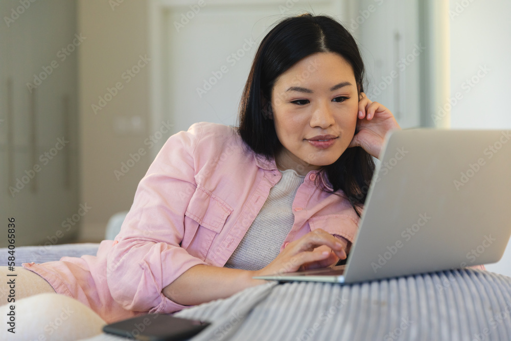 Happy asian woman sitting on beanbag at home using laptop, smiling Happy asian woman sitting on beanbag at home using laptop, smiling