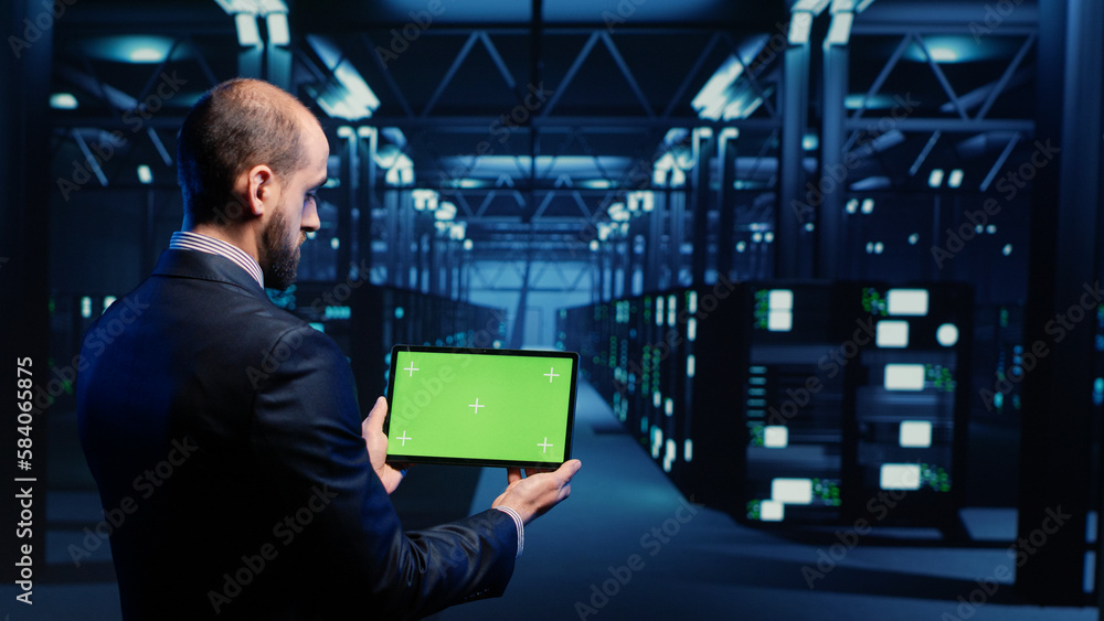 System engineer checking green screen display on tablet, running mainframe diagnostics in data center. IT administrator using copyspace display with blank chroma key, ai concept. Tripod shot. System engineer checking green screen display on tablet, running mainframe diagnostics in data center. IT administrator using copyspace display with blank chroma key, ai concept. Tripod shot.