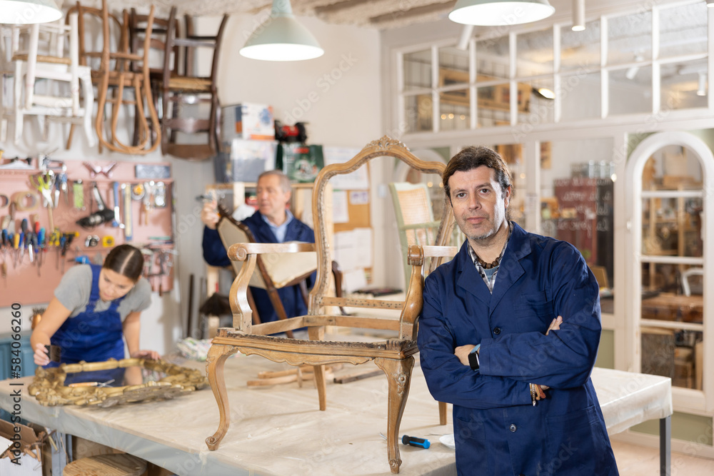 Portrait of middle-aged skillful repairman carpenter posing with crossed hands during workday in furniture woodwork studio