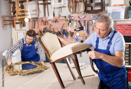 Professional furniture restorer in process of renovation vintage chair in workshop