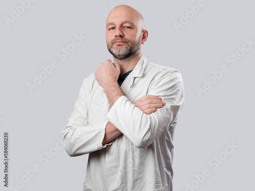 Portrait of a doctor on light color background. Male in 40s with grey beard in clinic uniform with stethoscope. Open friendly face. Hands crossed. © mark_gusev
