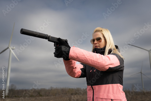 Quadro su tela A girl in sunglasses shoots with a pistol with a silencer at an outdoor shooting range