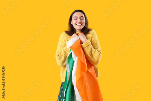 Happy young woman with flag of Ireland on yellow background