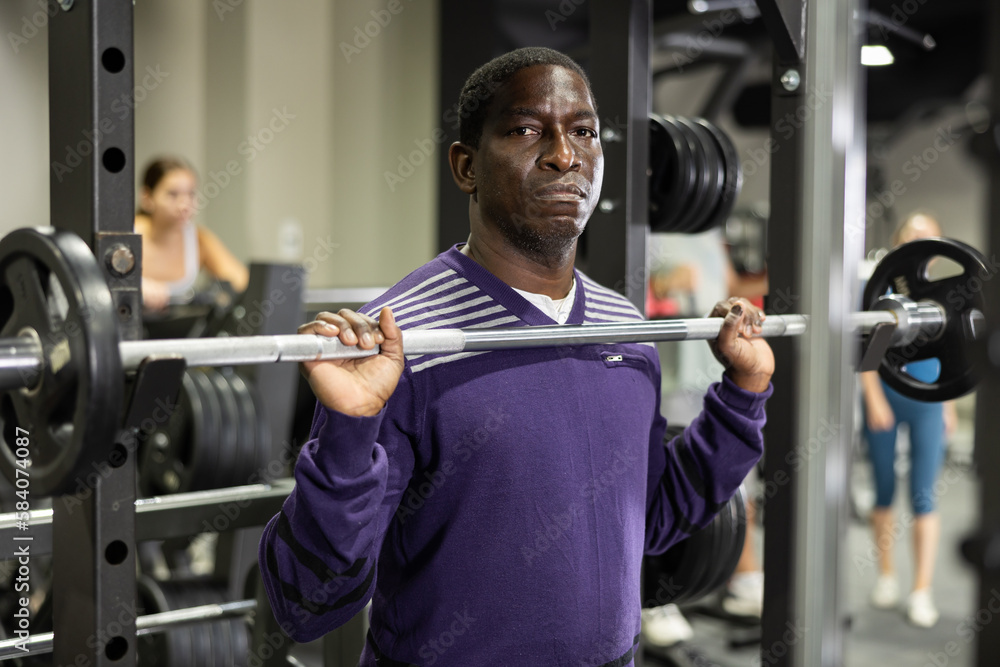 Fototapeta premium African-american man training with barbell using squat rack in gym