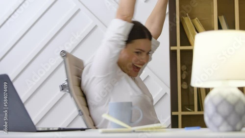 A young woman female worker at home in the office happy spins on the chair laughs spread her arms up close-up