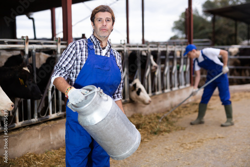 Dairy farmer man carrying aluminum can of milk in cowshed