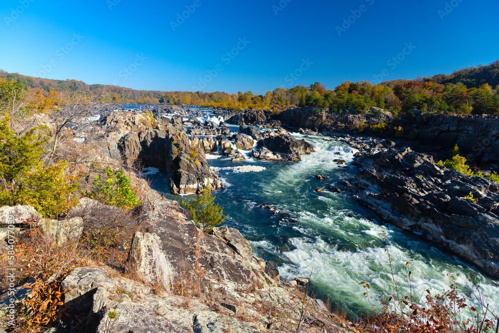 Severe rapid mountain river flows among high rocks. Autumn landscape of a wide mountain river on a sunny day.