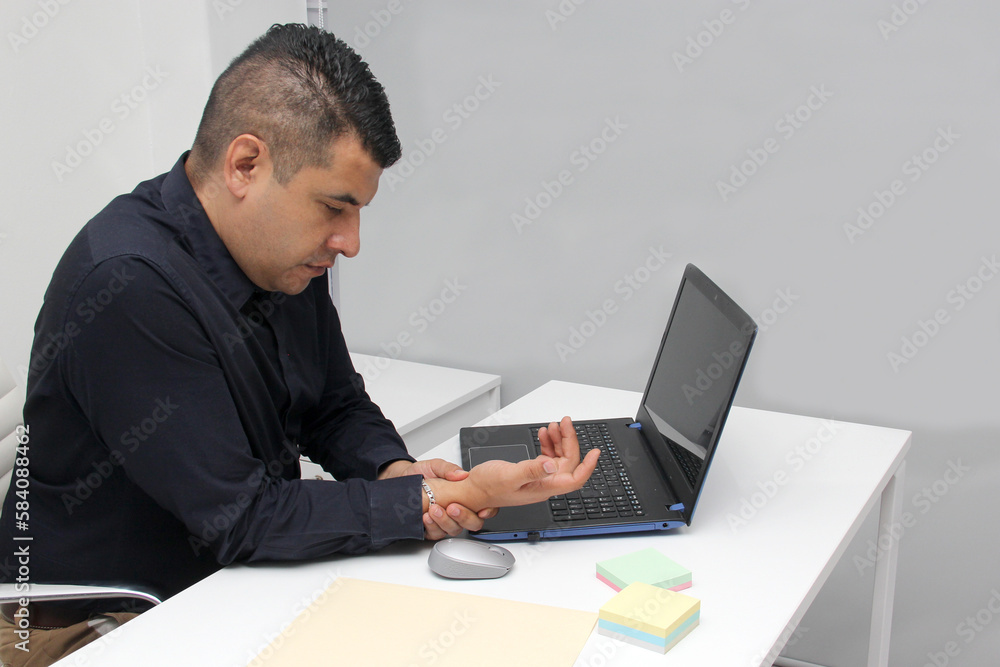 Adult Latin man suffering from pain, tingling, numbness and weakness in his wrist due to Carpal Tunnel Syndrome while working in his office with his laptop and mouse Adult Latin man suffering from pain, tingling, numbness and weakness in his wrist due to Carpal Tunnel Syndrome while working in his office with his laptop and mouse