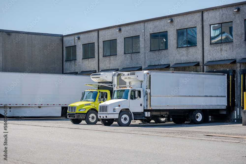 Affordable middle duty rigs semi trucks with refrigerated box trailers loading cargo standing in warehouse dock