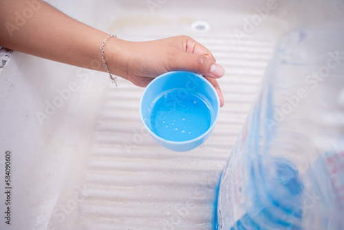 A young woman is holding a cup filled with blue liquid detergent on a traditional sink