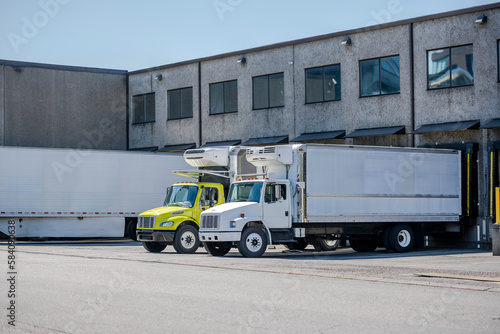 Affordable middle duty rigs semi trucks with refrigerated box trailers loading cargo standing in warehouse dock © vit