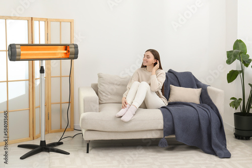 Woman warming near electric infrared heater indoors