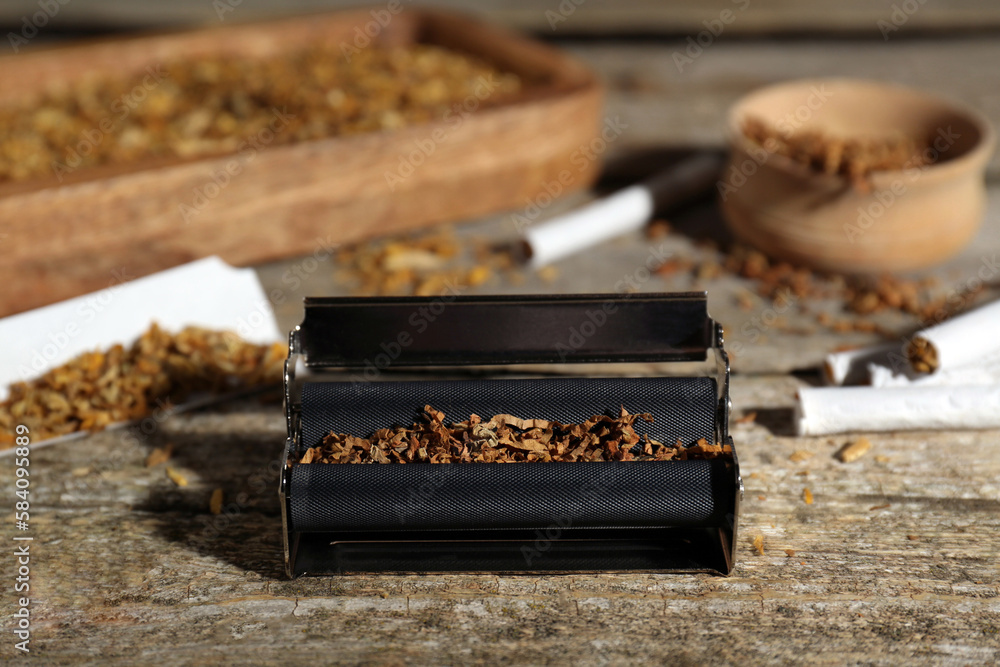 Roller with tobacco on old wooden table. Making hand rolled cigarettes Roller with tobacco on old wooden table. Making hand rolled cigarettes
