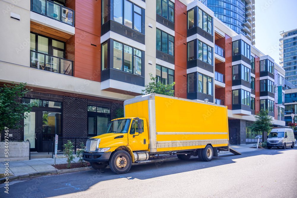 Obraz premium Yellow middle duty rig semi truck with box trailer and cargo mini van make a delivery to urban city apartment residential multi storey buildings