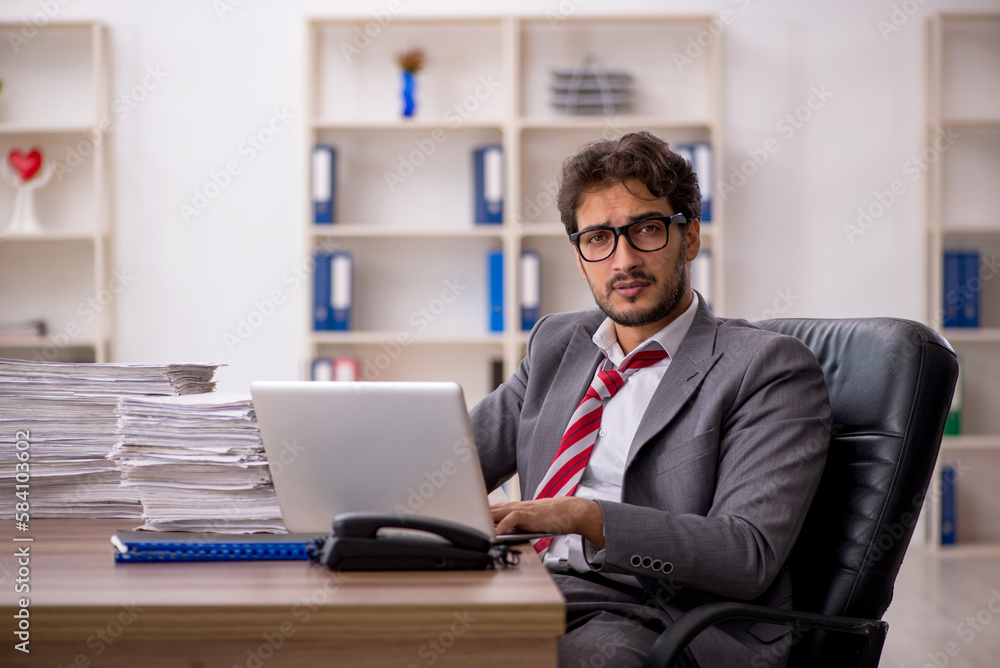 Young male employee unhappy with excessive work in the office Young male employee unhappy with excessive work in the office