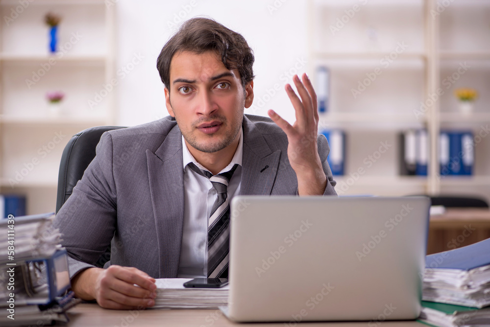 Young male employee unhappy with excessive work in the office Young male employee unhappy with excessive work in the office