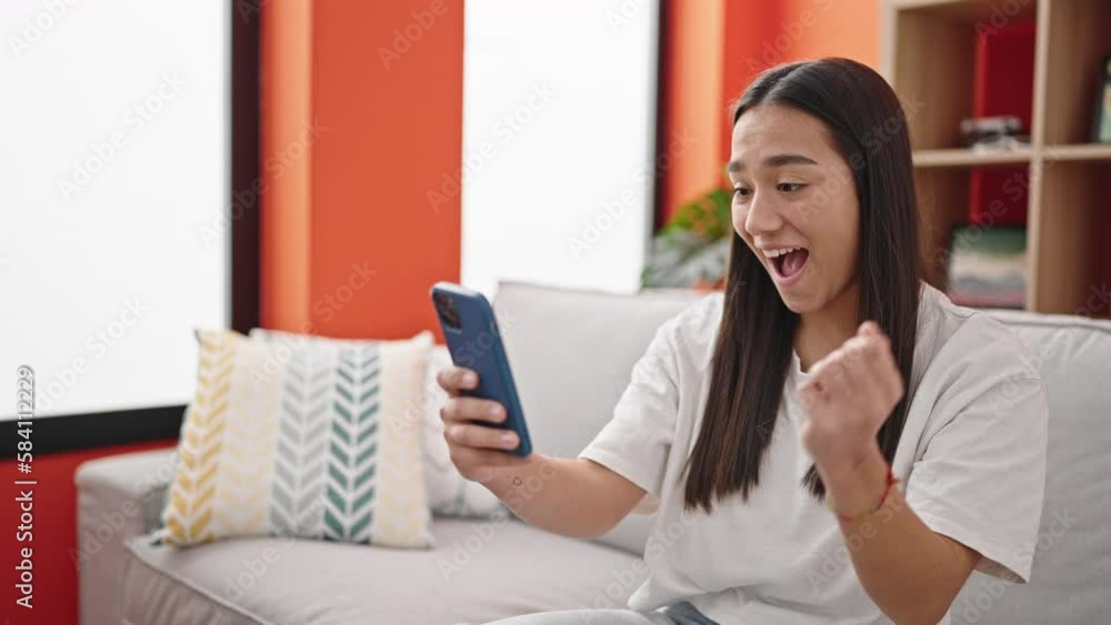 Young beautiful hispanic woman using smartphone with winner expression at home Young beautiful hispanic woman using smartphone with winner expression at home