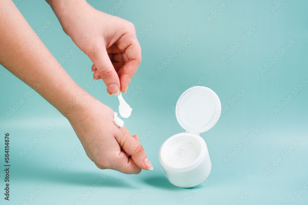 Face cream in a white jar on a blue background. Young woman holds cream in her hands. Closeup Skincare Product for facial. Woman applying cream on her hand Face cream in a white jar on a blue background. Young woman holds cream in her hands. Closeup Skincare Product for facial. Woman applying cream on her hand
