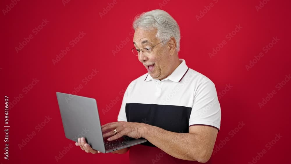 Middle age man with grey hair standing using laptop doing thumbs up over isolated red background Middle age man with grey hair standing using laptop doing thumbs up over isolated red background