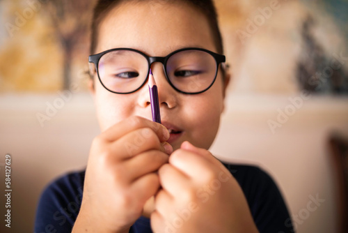 Smart young Asian boy wearing glasses squints at the pencil. The vision diseases problem. photo