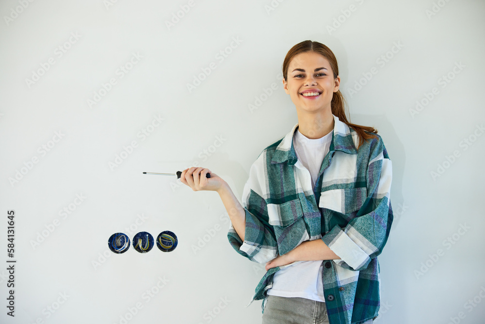 happy, smiling woman stands with a screwdriver and fixes sockets on a light wall happy, smiling woman stands with a screwdriver and fixes sockets on a light wall