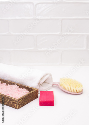 Towel, body brush, soap, sea salt on white bathroom background. Concept of self care, bath, spa. Copy space