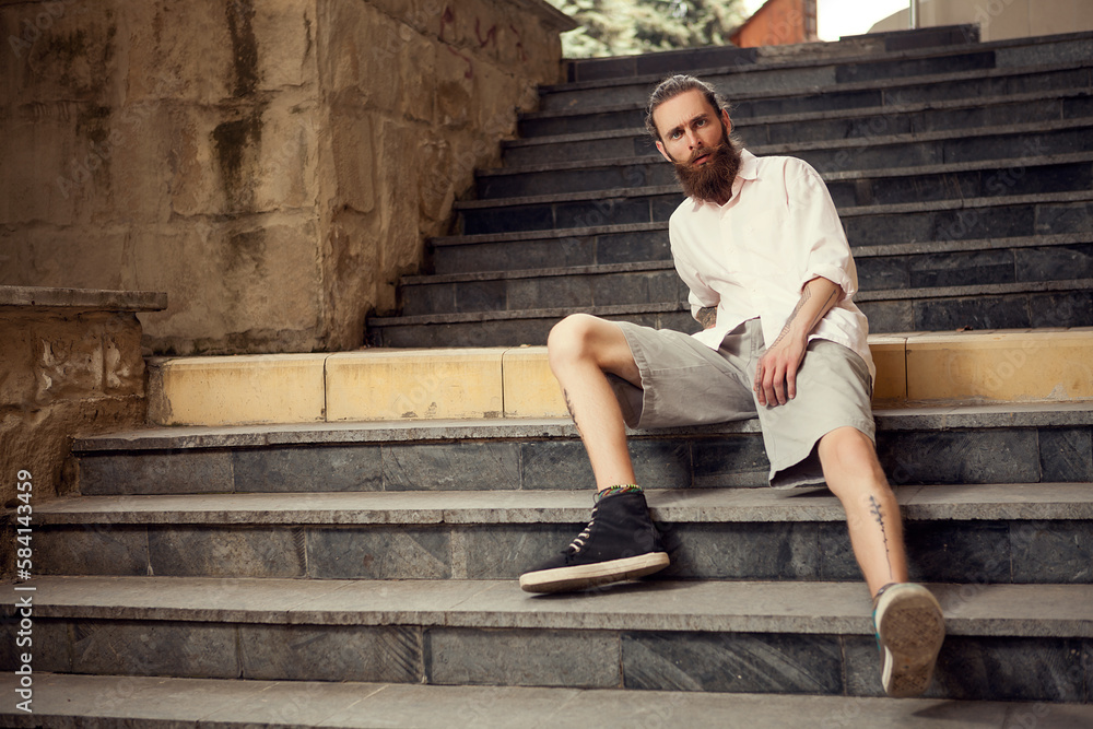 Cool looking hipster sitting in street on stairs looking at the camera Cool looking hipster sitting in street on stairs looking at the camera