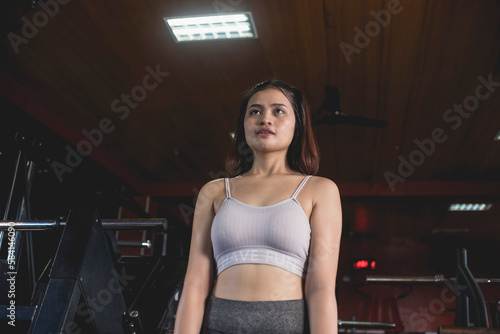A young asian woman in a white crop top and gray yoga pants looking at the mirror at the gym. Candid scene, low angle view.
