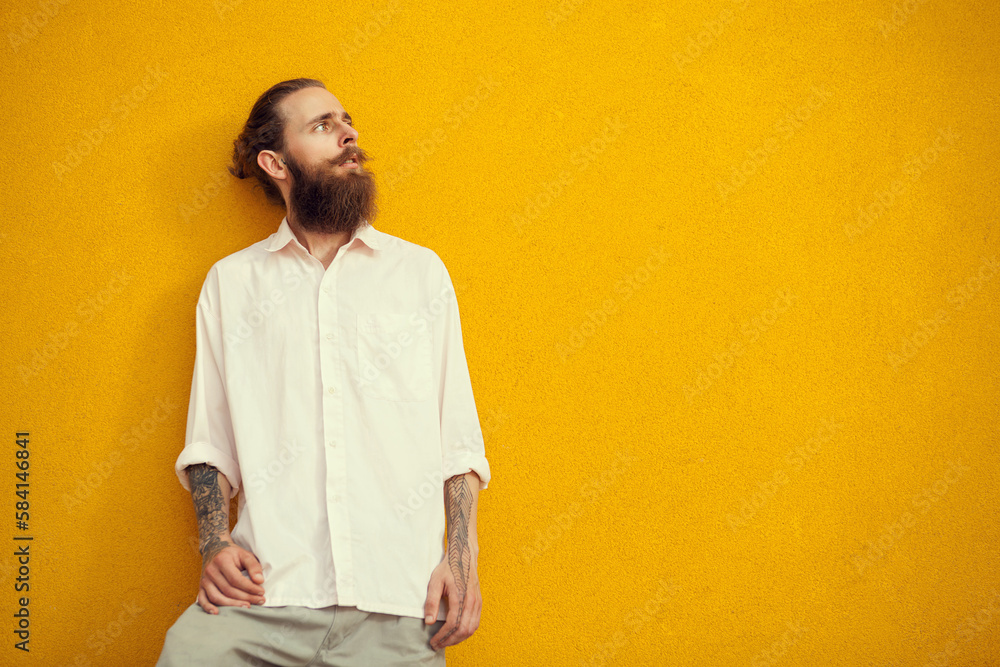 Bearded and tattooed man posing on yellow wall outside. Fashion and style Bearded and tattooed man posing on yellow wall outside. Fashion and style
