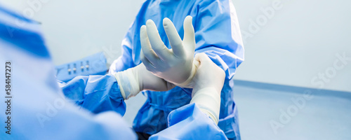 Nurse or doctor put surgical glove on surgeon 's hand inside operating room in hospital.People in blue sterile gown in theatre prepare for surgery.Medical glove to protection.Space blur background.
