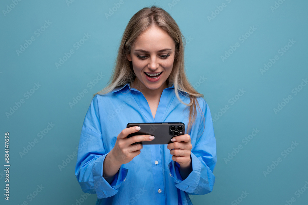horizontal photo of a funny charming blonde girl with a smartphone in her hands on an isolated blue background horizontal photo of a funny charming blonde girl with a smartphone in her hands on an isolated blue background