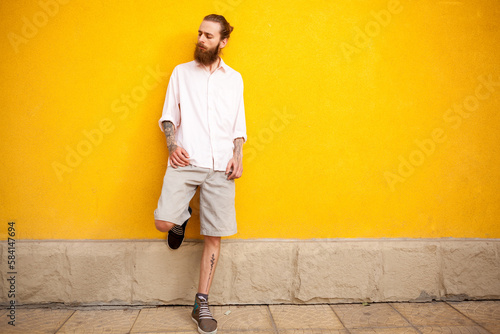 Tattooed bearded man on yellow wall posing outdoor