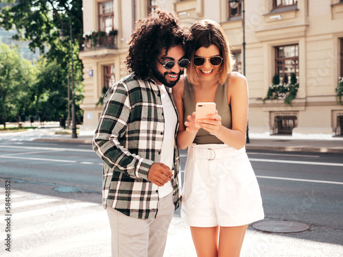 Smiling beautiful woman and her handsome boyfriend. Happy cheerful family. Woman having fun. Sexy couple posing in the street at sunny day. Using smartphone apps, looking at cellphone screen