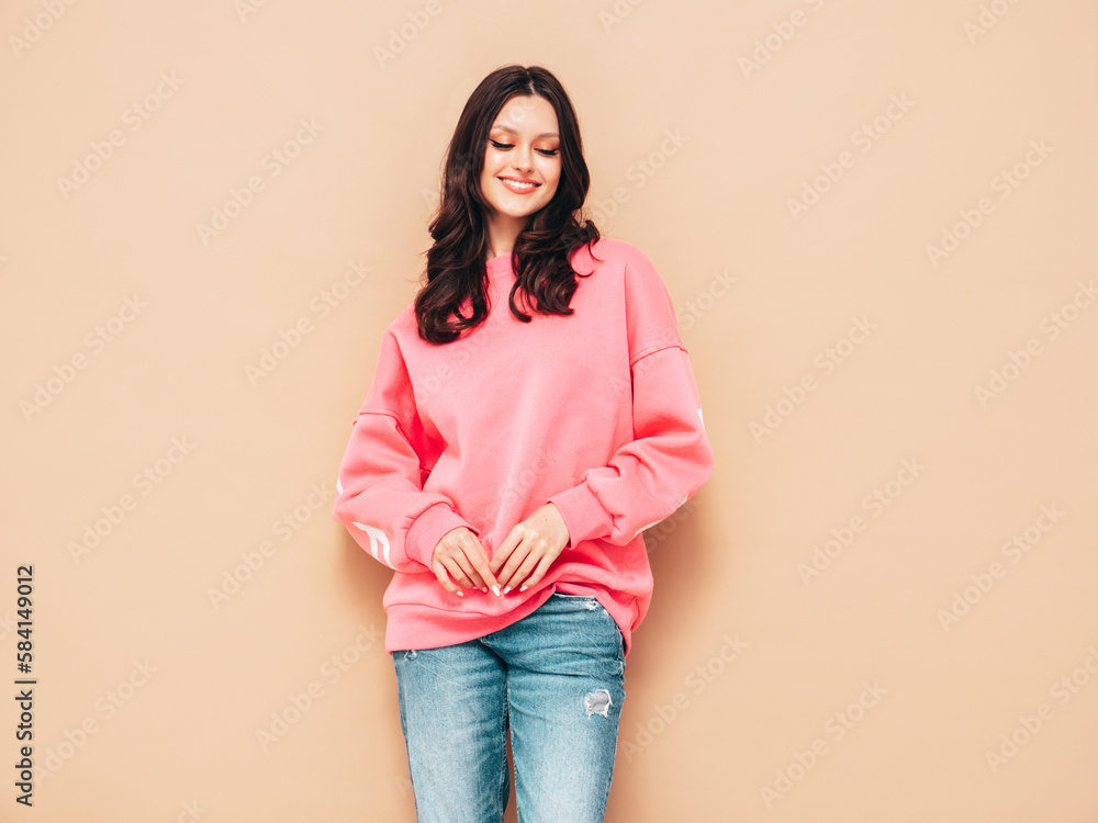 Young beautiful smiling female in trendy summer jeans and pink sweater clothes. Sexy carefree woman posing near beige wall in studio. Positive model. Cheerful and happy Young beautiful smiling female in trendy summer jeans and pink sweater clothes. Sexy carefree woman posing near beige wall in studio. Positive model. Cheerful and happy