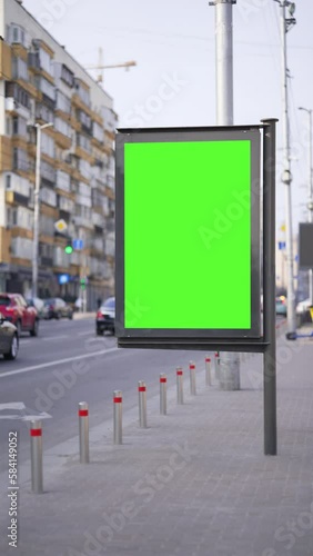Vertical Screen: Green screen billboard with city traffic background. Blurred transport moving on road. Vertical lightbox for advertising, cars driving in town