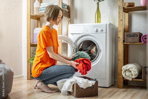 Woman is puting multicolor clothes into the washing machine in the laundry room. The concept of caring for things, cleaning and hygiene